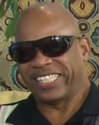 Bold black man with a dark sunglasses and a big toothy smile.