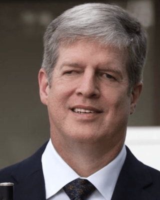 Middle-aged man smiling with grey hair, in a dark suit is holding a white cane